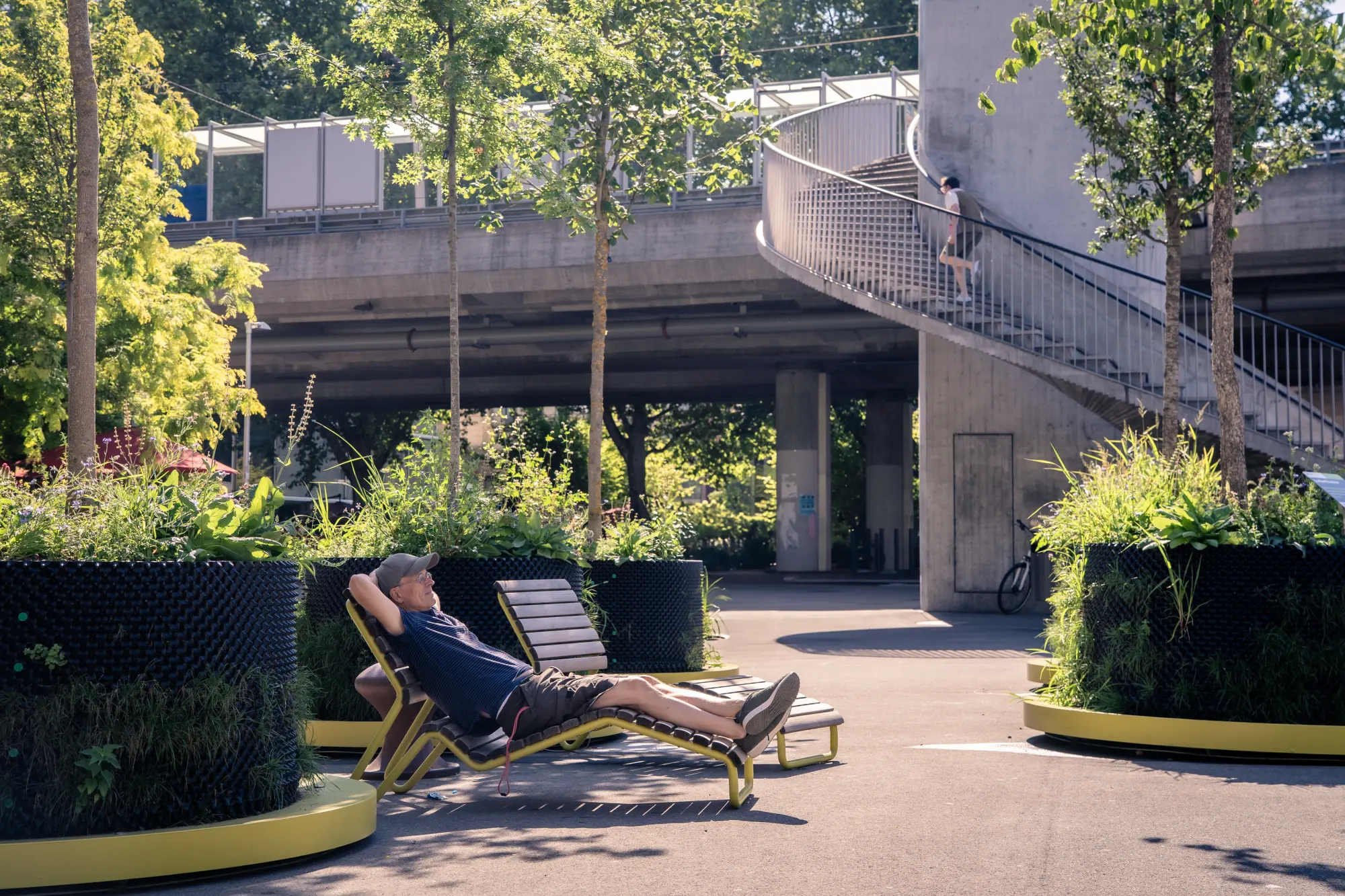 Mann entspannt auf Liegestuhl zwischen mobilen Baumpflanzgefässen auf dem Schiffbauplatz in Zürich, im Hintergrund Wendeltreppe.
