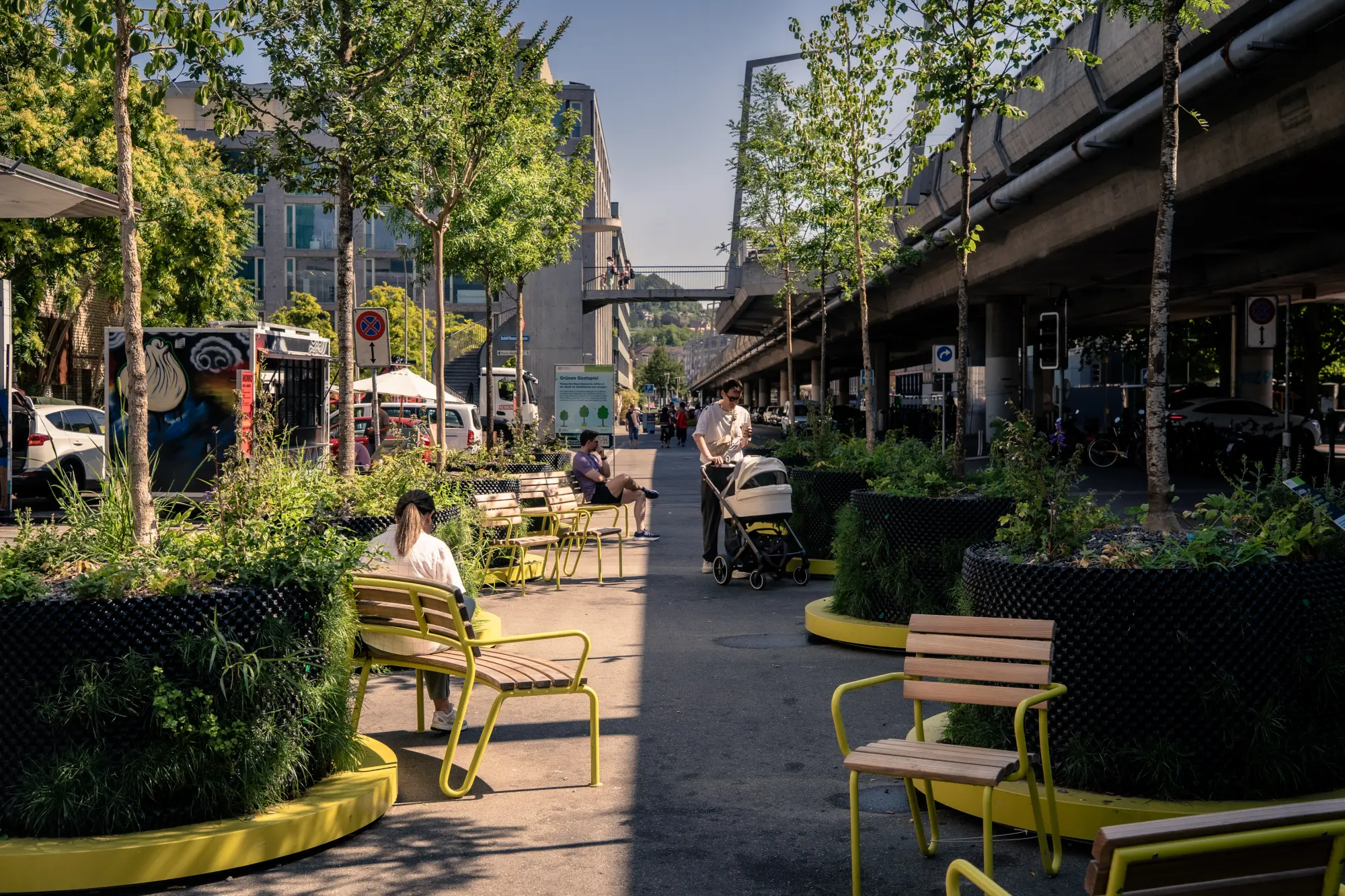 Fußgängerpassage unter der Hardbrücke in Zürich mit mobilen Baumpflanzgefässen, Sitzbänken und Sesseln als temporäre Begrünung.