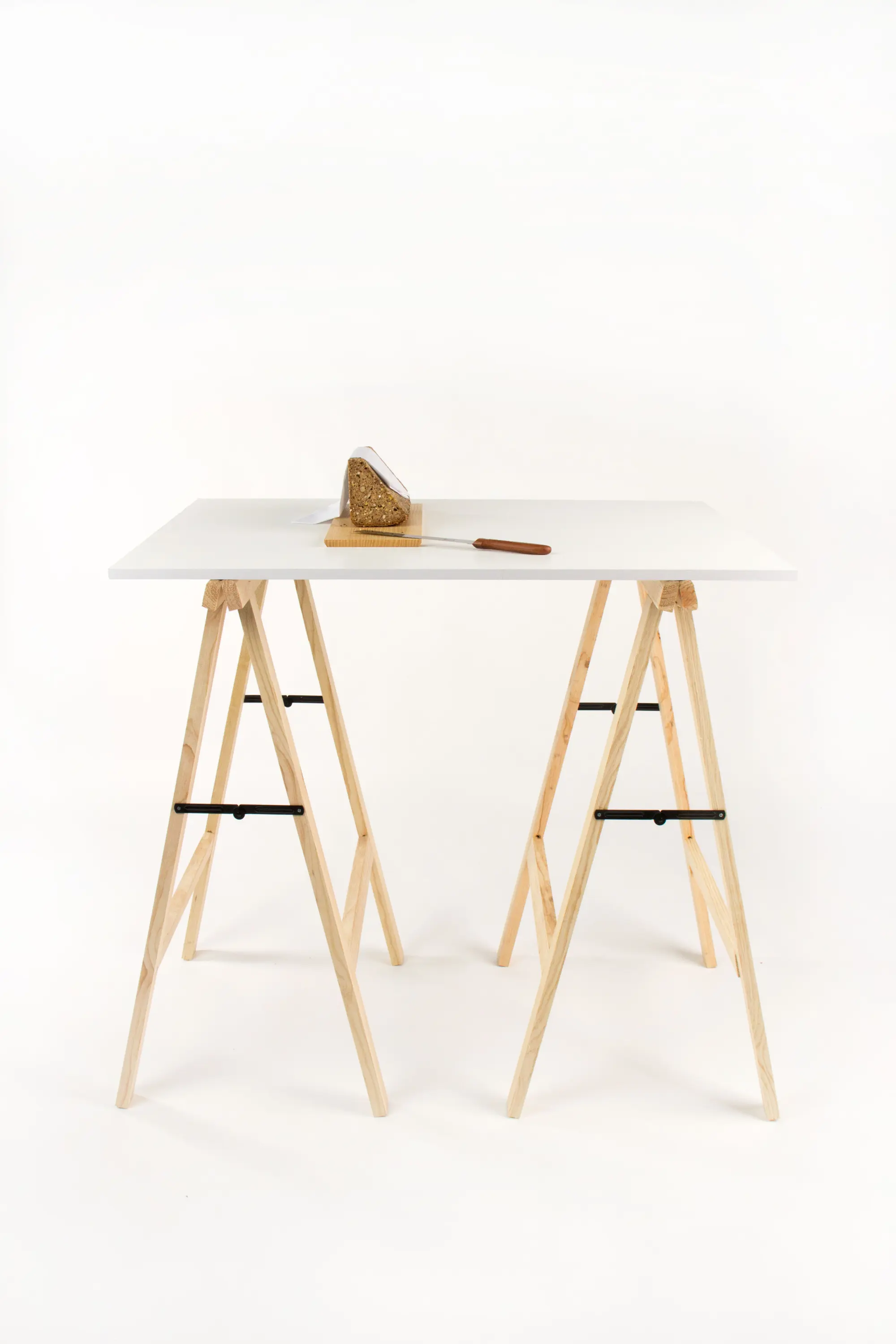 Minimalistischer Tisch aus Holz und weisser Tischplatte mit angeschnittenem Mehrkornbrot in dreieckiger Form auf einem hellen Holzbrett und Brotmesser.