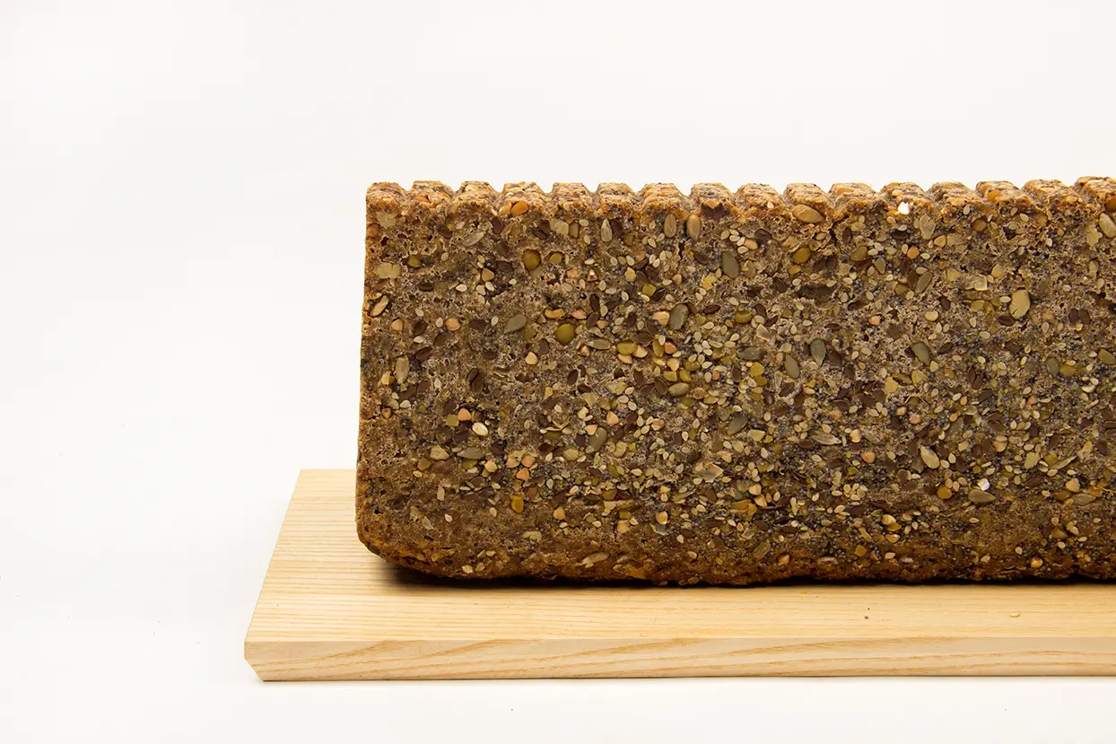 Gestaltetes Mehrkornbrot mit Saaten und geriffelter Oberseite auf einem hellen Holzbrett.